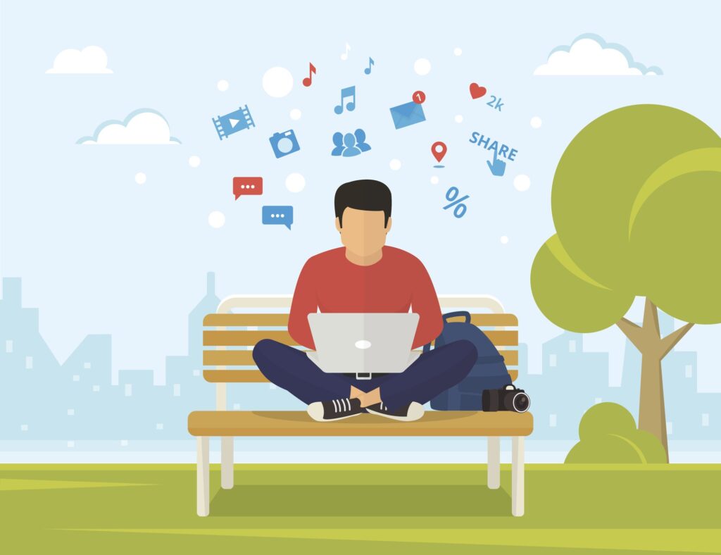 Young man sitting in the park on the bench and working with laptop