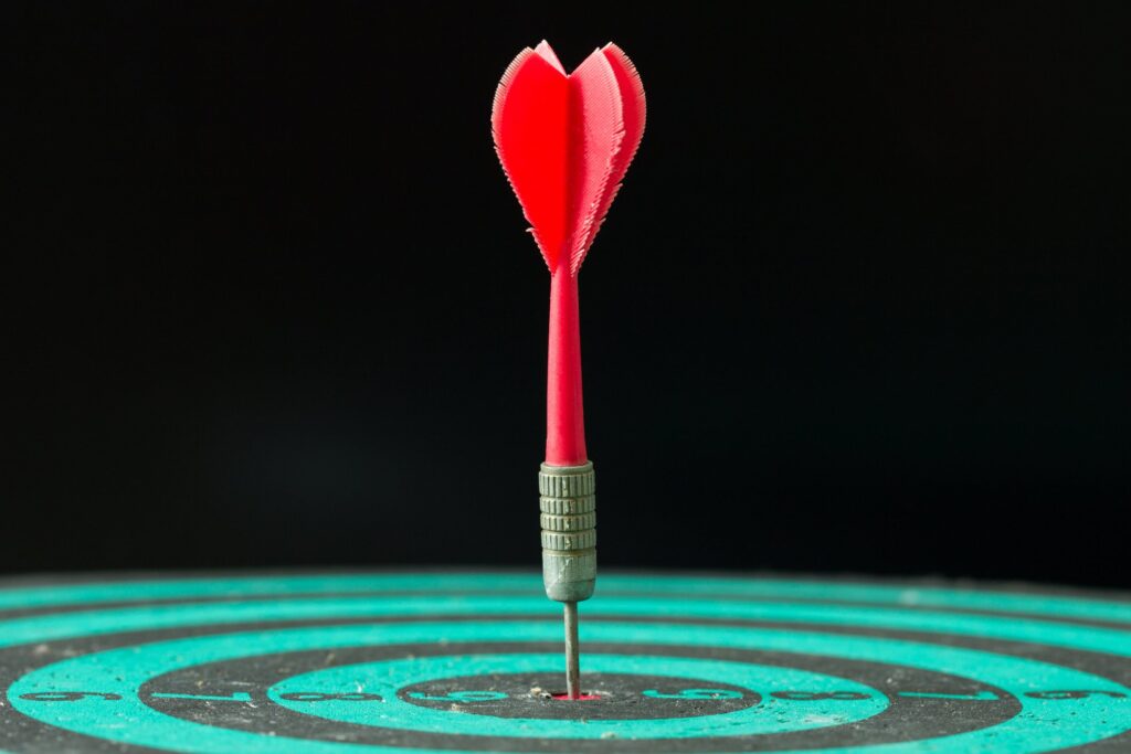 Red dart arrow hitting in the center of green dartboard.